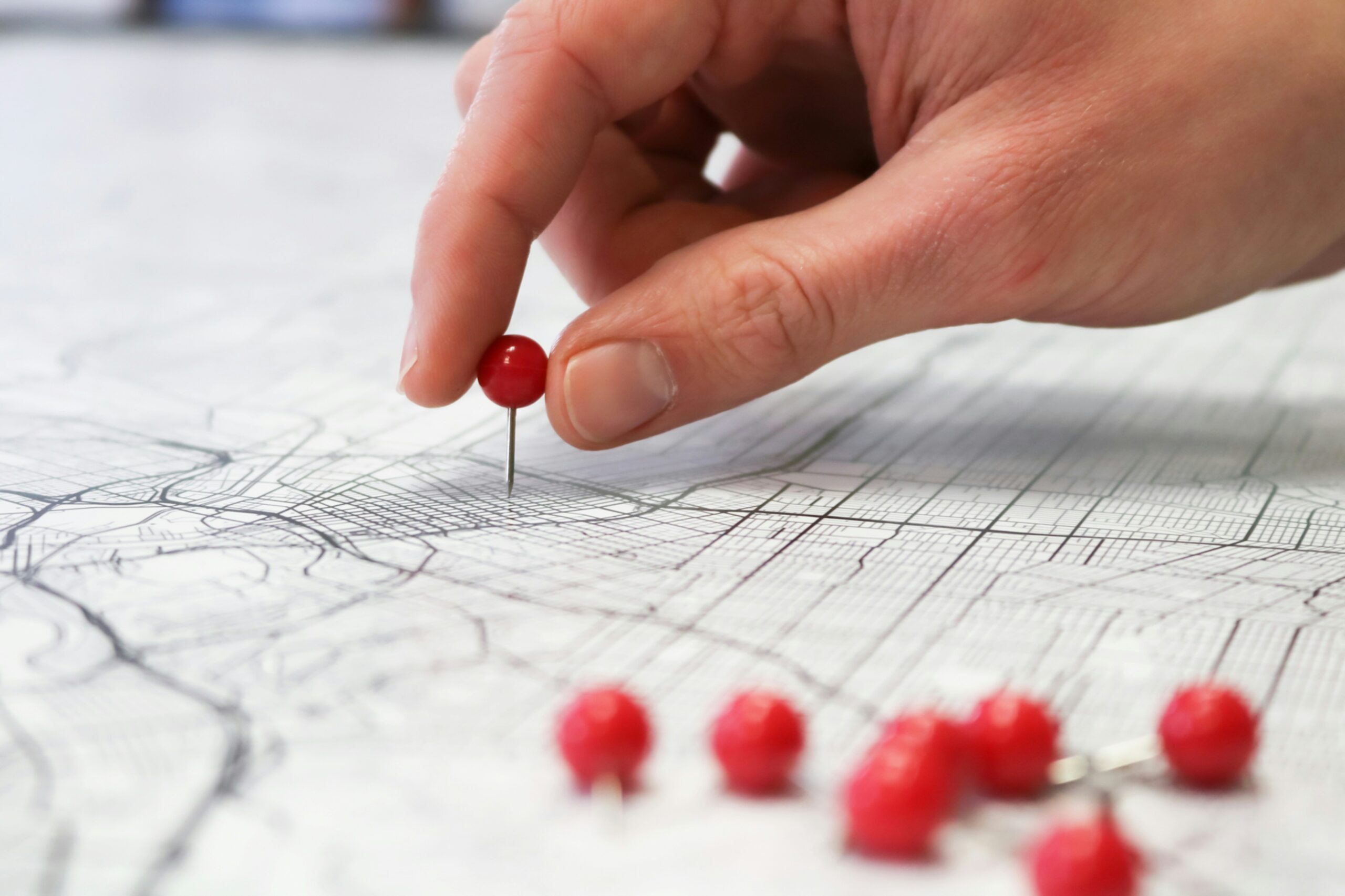 Close-up of hand placing red pins on a printed map, symbolising planning and tracking referral activity across regions.